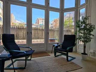 Praxisraum in der C/ Balmes 76: zwei Sessel vor einer hellen Fensterfront mit Blick auf eine Terrasse
